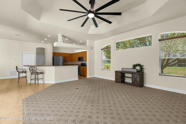 living room with baseboards, visible vents, a raised ceiling, and a ceiling fan