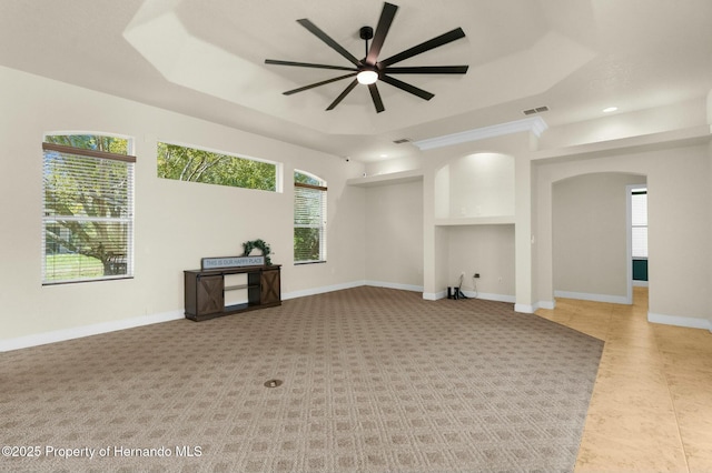 unfurnished living room featuring arched walkways, a ceiling fan, visible vents, baseboards, and a tray ceiling