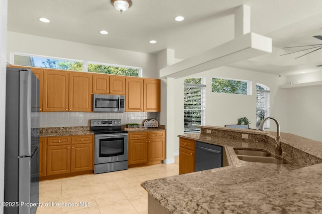 kitchen featuring appliances with stainless steel finishes, backsplash, a sink, and light stone counters