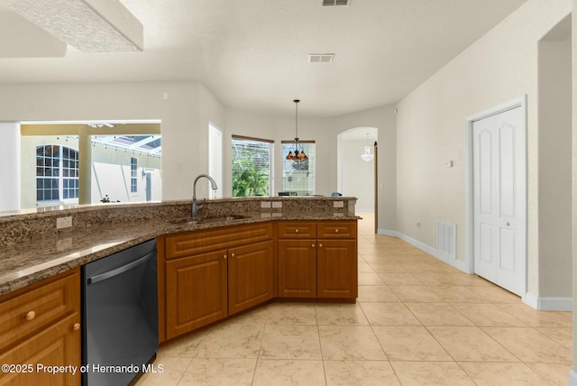 kitchen featuring visible vents, dark stone counters, dishwashing machine, brown cabinets, and a sink