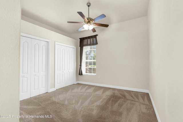 unfurnished bedroom featuring baseboards, carpet flooring, a ceiling fan, and multiple closets