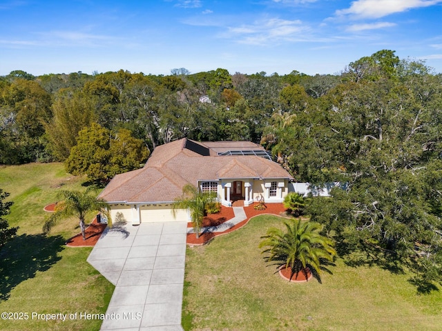 view of front of property with driveway, a shingled roof, a forest view, an attached garage, and a front lawn