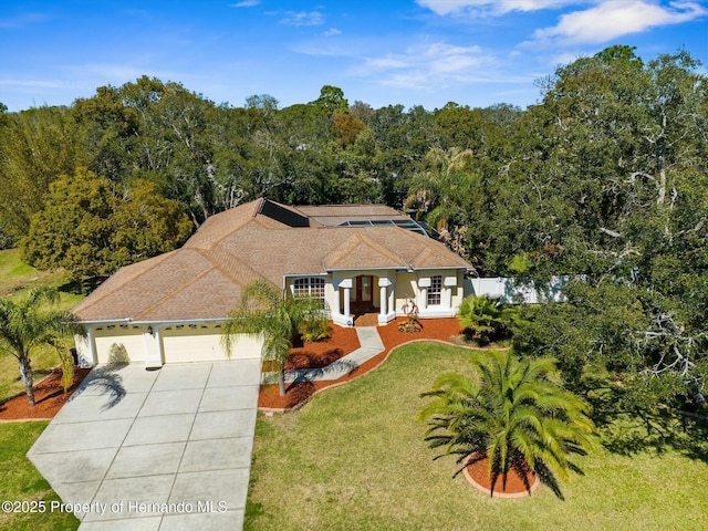 view of front facade featuring concrete driveway, an attached garage, fence, a wooded view, and a front yard