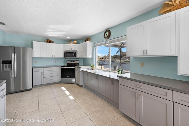 kitchen with a textured ceiling, stainless steel appliances, light tile patterned flooring, and white cabinets