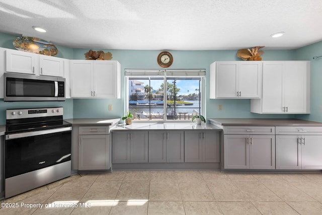 kitchen with light tile patterned floors, appliances with stainless steel finishes, gray cabinets, a textured ceiling, and white cabinetry