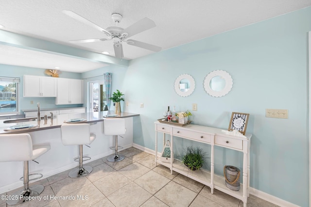 kitchen with light tile patterned floors, ceiling fan, a breakfast bar, a sink, and white cabinetry