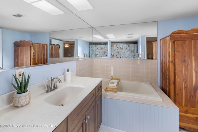 full bathroom featuring a relaxing tiled tub, visible vents, and vanity