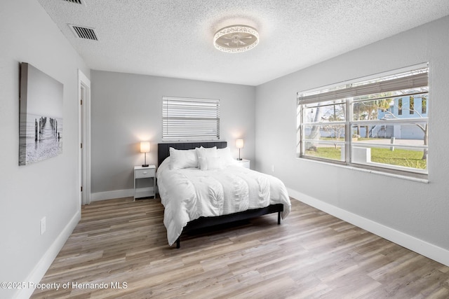 bedroom featuring light wood-style floors, visible vents, a textured ceiling, and baseboards