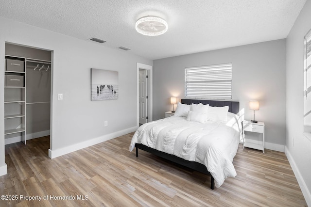 bedroom with light wood-style floors, visible vents, a spacious closet, and baseboards