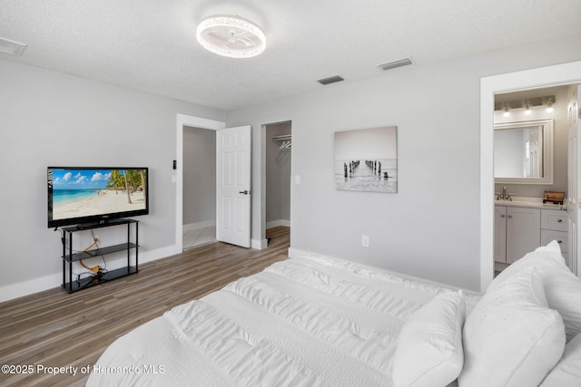 bedroom featuring a textured ceiling, ensuite bath, wood finished floors, and visible vents