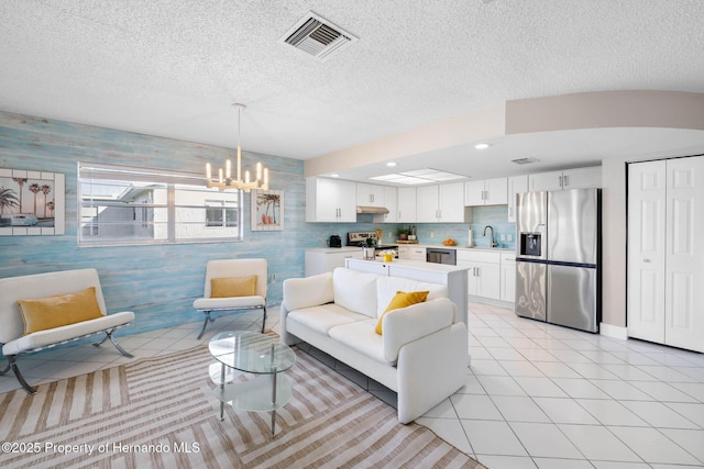 living room featuring visible vents, a textured ceiling, wallpapered walls, and light tile patterned floors