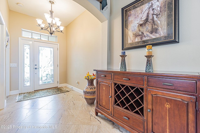 foyer featuring arched walkways, marble finish floor, an inviting chandelier, and baseboards