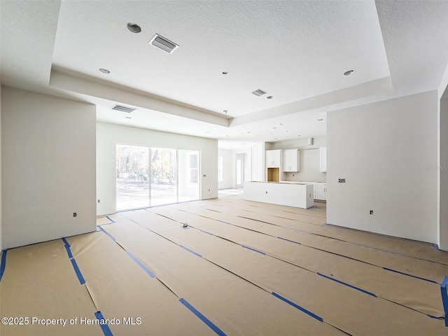 unfurnished living room featuring a tray ceiling and visible vents