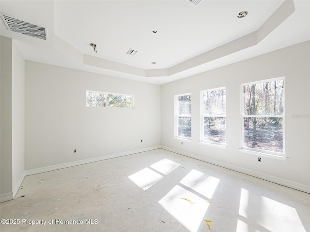 empty room with a tray ceiling, visible vents, and baseboards