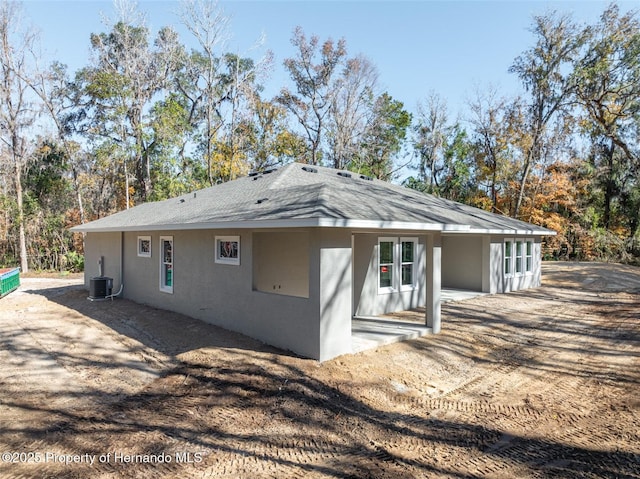 view of side of home featuring a patio, a shingled roof, and stucco siding