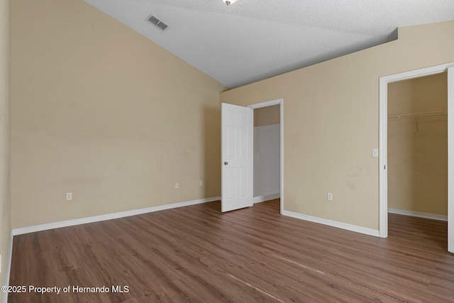 unfurnished bedroom with vaulted ceiling, a spacious closet, wood finished floors, and visible vents