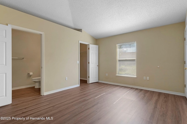 unfurnished bedroom with lofted ceiling, a closet, a spacious closet, a textured ceiling, and wood finished floors