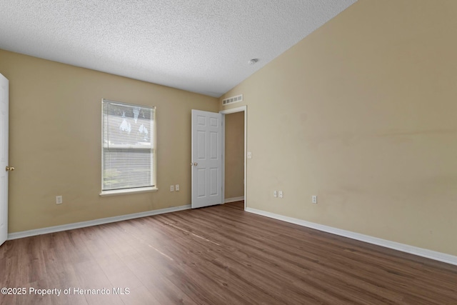 empty room with lofted ceiling, a textured ceiling, visible vents, and wood finished floors