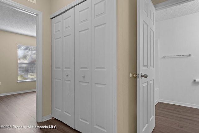 hallway featuring a textured ceiling, dark wood-style flooring, and baseboards