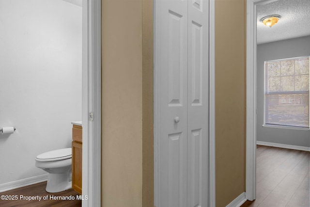 bathroom with a textured ceiling, toilet, wood finished floors, vanity, and a closet