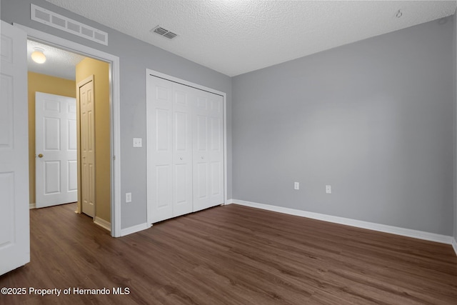 unfurnished bedroom with baseboards, a textured ceiling, visible vents, and dark wood-type flooring