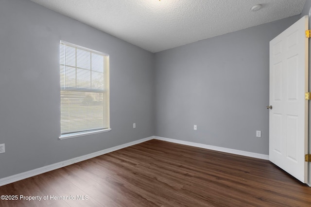 empty room featuring a textured ceiling, baseboards, and dark wood-type flooring