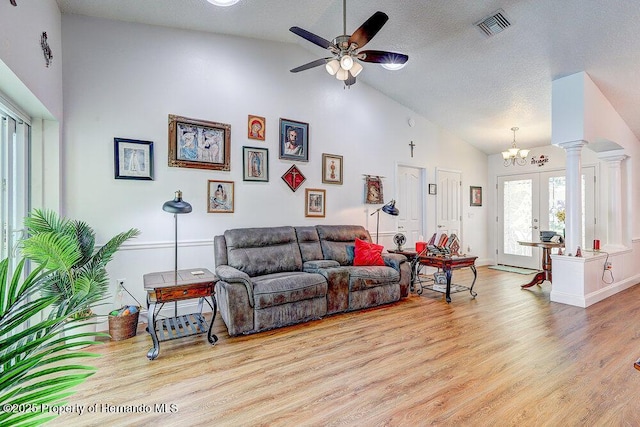 living area with visible vents, light wood-style flooring, a textured ceiling, ornate columns, and ceiling fan with notable chandelier