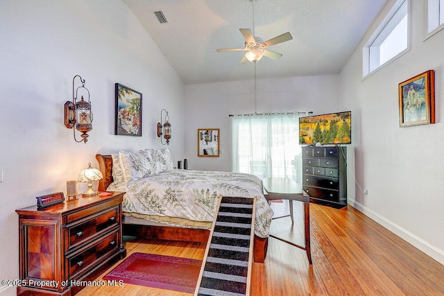 bedroom with baseboards, visible vents, wood finished floors, vaulted ceiling, and a textured ceiling