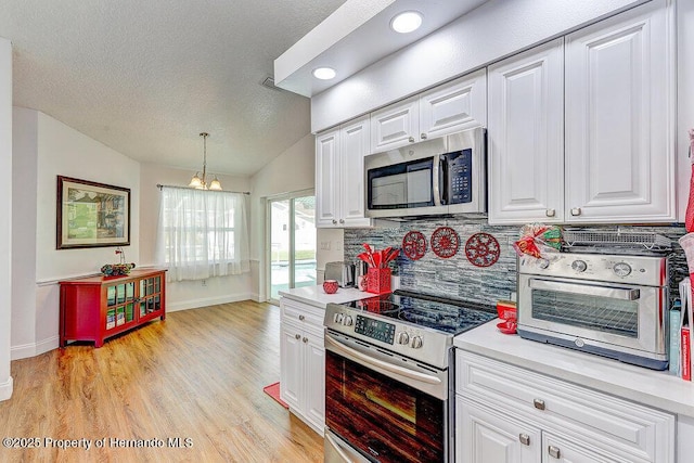 kitchen with stainless steel appliances, light countertops, light wood-style flooring, white cabinets, and vaulted ceiling