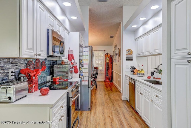 kitchen featuring light wood-style flooring, white cabinetry, stainless steel appliances, and a sink