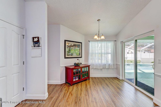 dining room with baseboards, an inviting chandelier, vaulted ceiling, a textured ceiling, and light wood-style floors