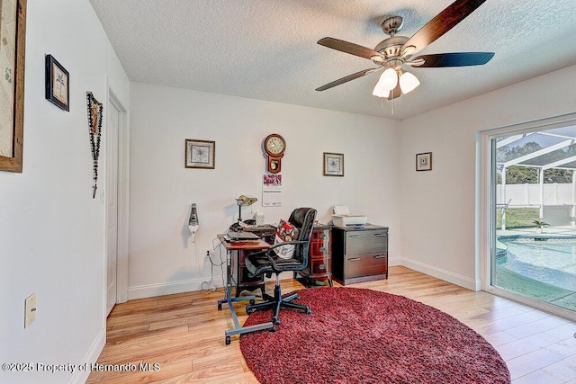 office area with a textured ceiling, baseboards, a ceiling fan, and light wood-style floors