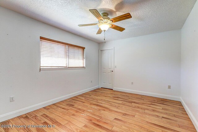 spare room with ceiling fan, light wood-style flooring, baseboards, and a textured ceiling