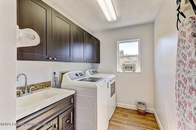 clothes washing area featuring light wood finished floors, cabinet space, a textured ceiling, washer and dryer, and baseboards