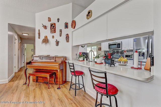 kitchen with a breakfast bar area, light wood finished floors, appliances with stainless steel finishes, white cabinets, and a peninsula