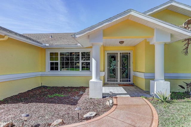 entrance to property with a shingled roof and stucco siding