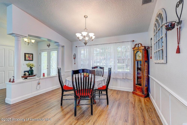 dining space featuring lofted ceiling, decorative columns, light wood-style flooring, and an inviting chandelier