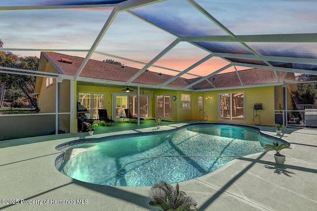 pool at dusk with ceiling fan, a patio, glass enclosure, and an outdoor pool