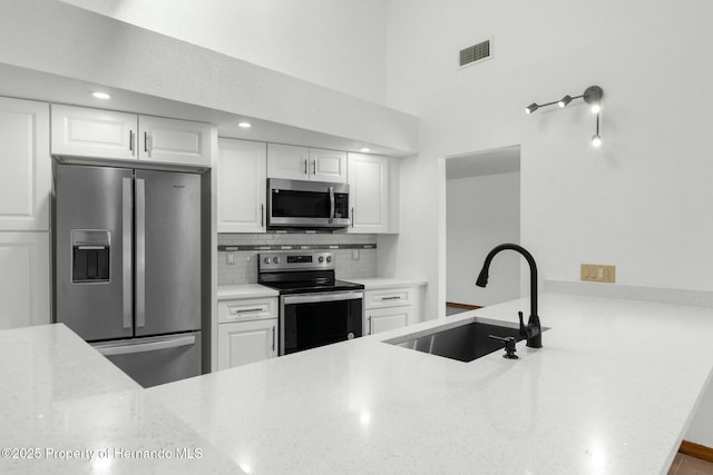 kitchen featuring visible vents, decorative backsplash, a peninsula, stainless steel appliances, and a sink