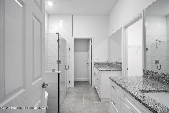 full bathroom featuring a shower stall, two vanities, baseboards, and a sink