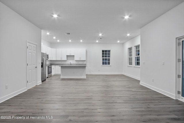 unfurnished living room with visible vents, baseboards, recessed lighting, wood finished floors, and a sink