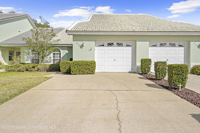 ranch-style house featuring driveway, a front lawn, a tile roof, and stucco siding