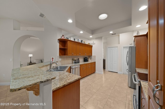 kitchen with a tray ceiling, stainless steel appliances, visible vents, a sink, and a peninsula