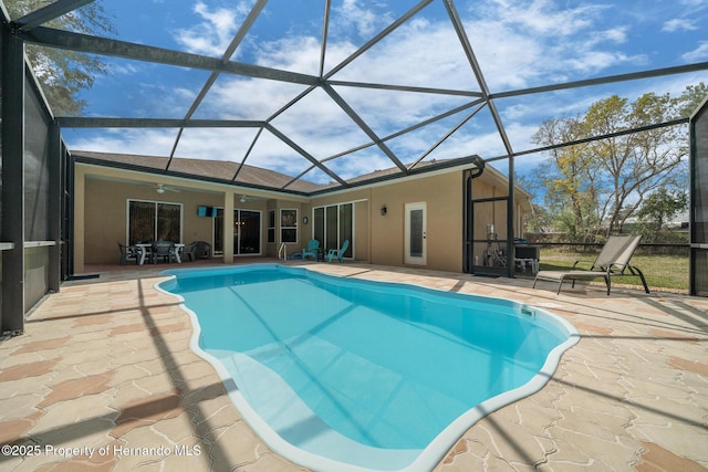 outdoor pool featuring glass enclosure, a patio area, and a ceiling fan