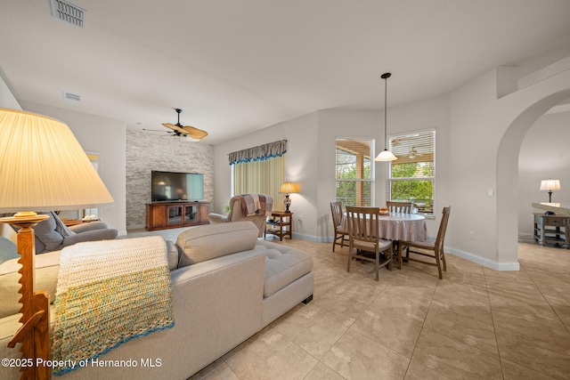 living room with arched walkways, ceiling fan, visible vents, and baseboards