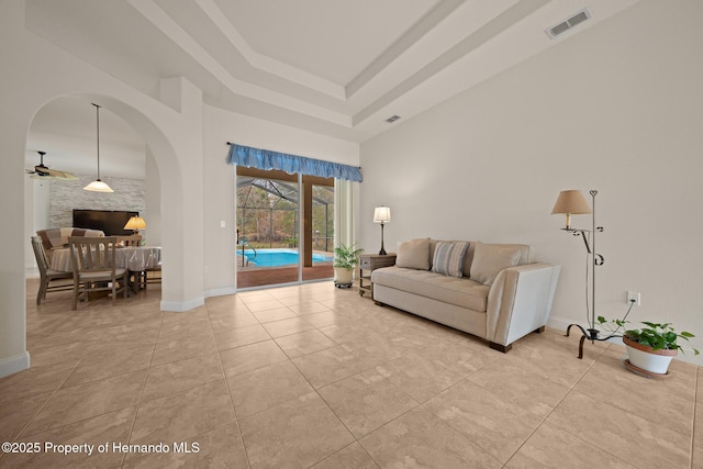 living area with light tile patterned floors, visible vents, a towering ceiling, a ceiling fan, and baseboards