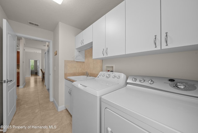 washroom featuring light tile patterned floors, cabinet space, visible vents, washing machine and dryer, and a sink