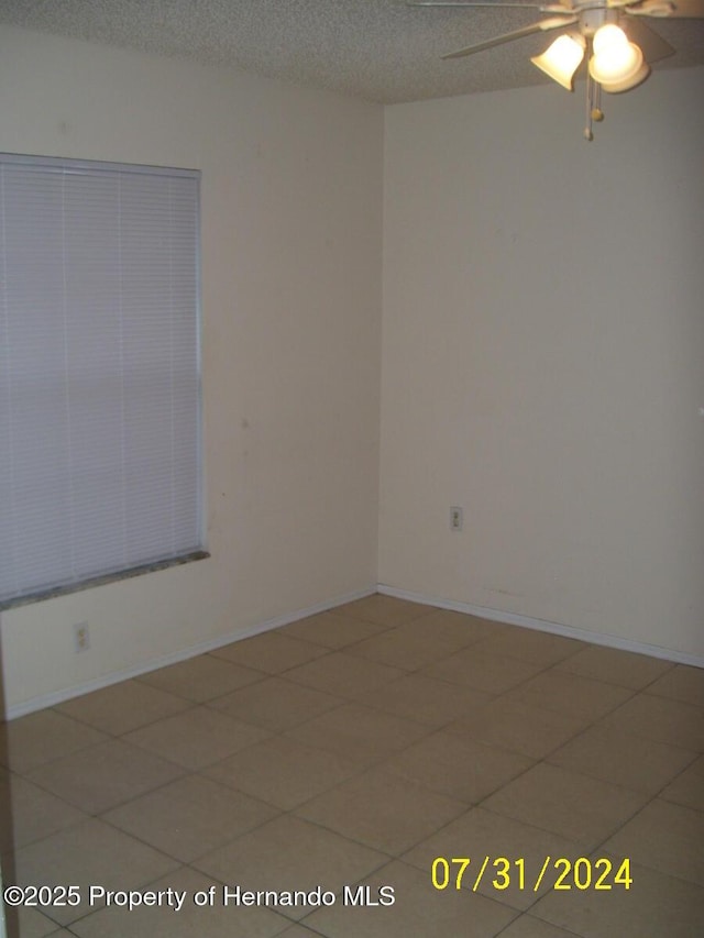 empty room with a textured ceiling, a ceiling fan, and baseboards