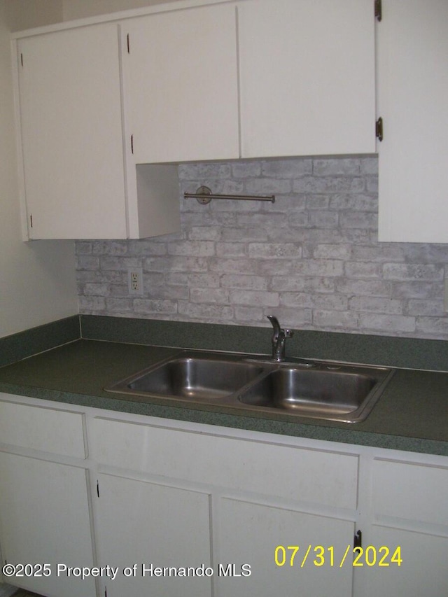 kitchen featuring backsplash, dark countertops, a sink, and white cabinetry