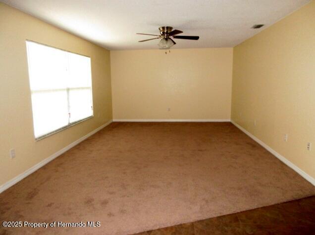 carpeted spare room featuring ceiling fan, visible vents, and baseboards